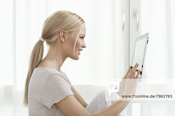 Young blond woman using tablet PC at home