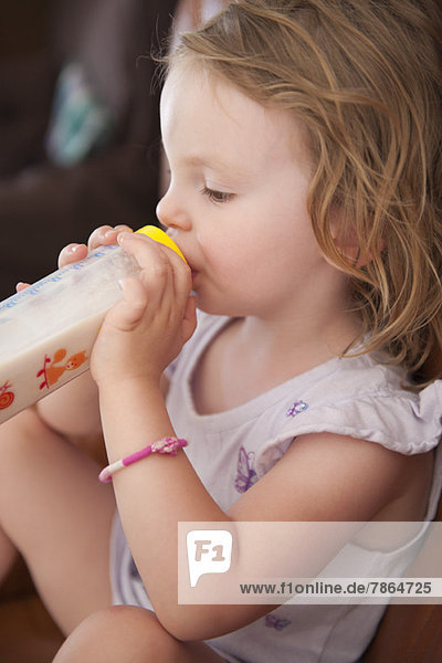Kleines Mädchen trinkt Milch aus der Flasche  Seitenansicht