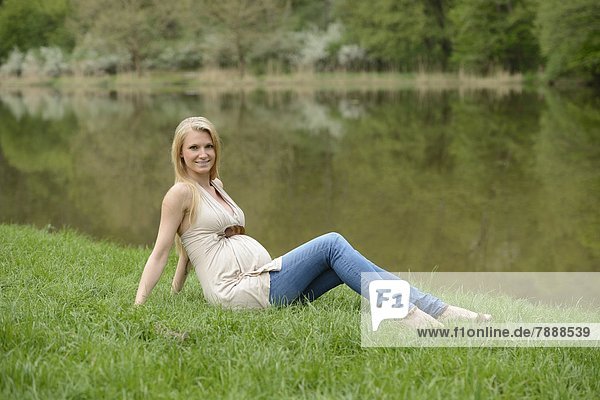 Junge schwangere Frau sitzt auf einer Wiese