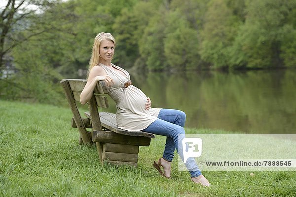 Junge schwangere Frau sitzt auf einer Bank