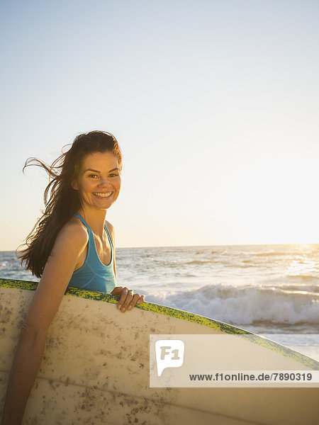 Mixed race woman carrying surfboard on beach