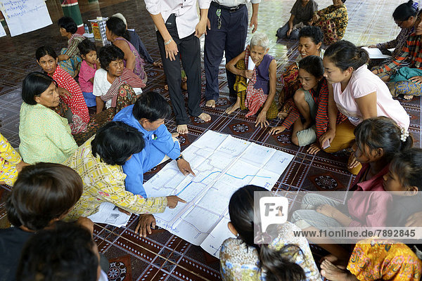 Men and women from the village discussing with representatives of a charity organization  over a map in which the springs and wells are located in their village  to analyze the problems and potentials of the water supply to the community