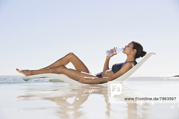 Schöne Frau trinkt Wasser am Strand