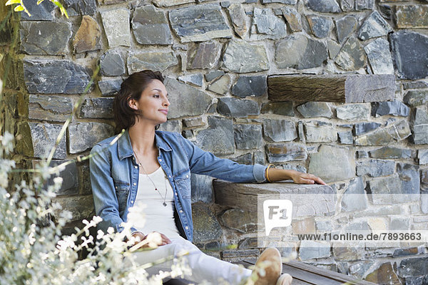 Woman leaning against a stone wall and day dreaming