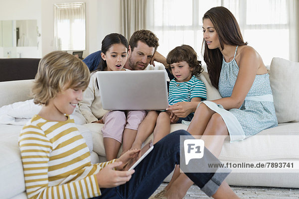 Familie mit elektronischen Geräten im Wohnzimmer