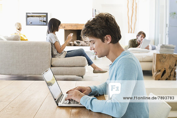 Mann mit einem Laptop und seinen Freunden mit elektronischen Gadgets im Hintergrund