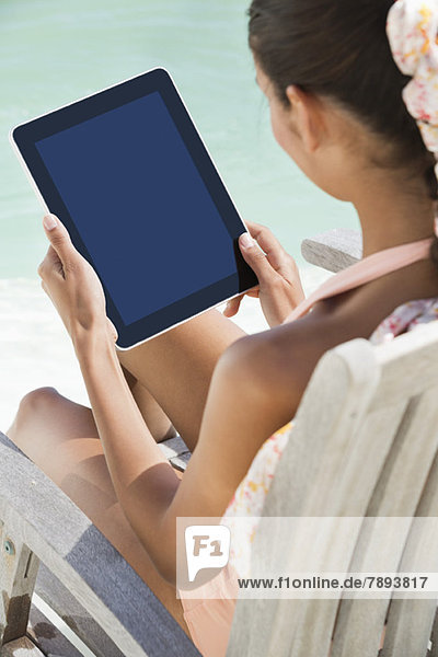Frau sitzt auf einem Stuhl und benutzt ein digitales Tablett am Strand.