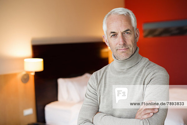 Porträt eines Mannes mit gekreuzten Armen in einem Hotelzimmer