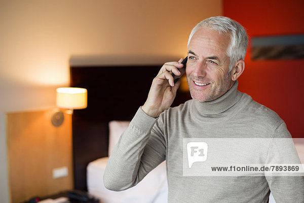 Ein Mann  der auf einem Handy in einem Hotelzimmer spricht.