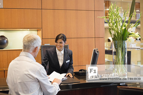 Geschäftsmann im Gespräch mit einer Rezeptionistin an der Hotelrezeption