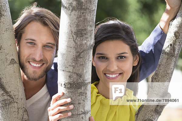 Portrait of a couple smiling behind a tree