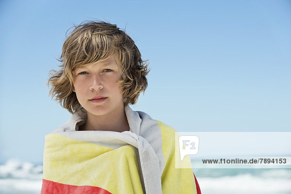 Porträt eines in ein Handtuch gewickelten Jungen am Strand