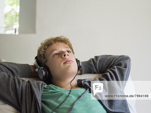 Teenager-Junge auf dem Bett liegend und Musik hörend