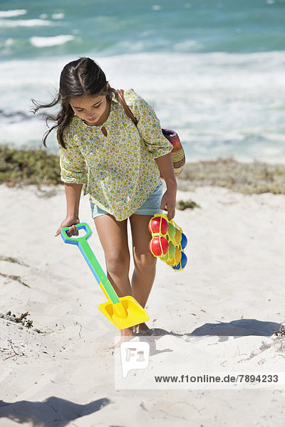 Mädchen mit Schaufel und Spielzeug am Strand
