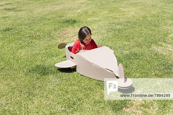 Mädchen beim Spielen mit einem Flugzeug aus Pappe im Rasen