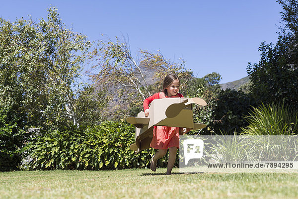 Mädchen beim Spielen mit einem Flugzeug aus Pappe im Rasen