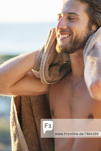 Glücklicher Mann wischt sich mit einem Handtuch am Strand ab
