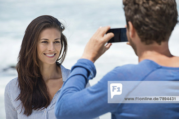 Mann fotografiert seine Frau mit einem Handy am Strand