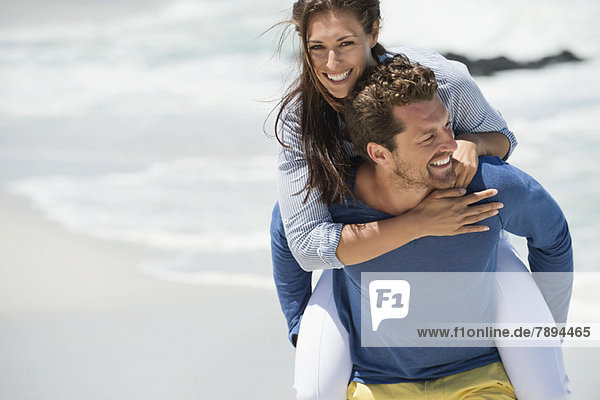 Man giving piggyback ride to his wife on the beach
