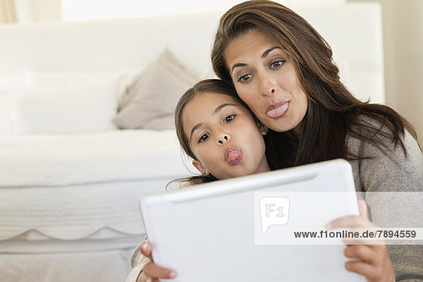 Woman and her daughter making their faces in front of digital tablet