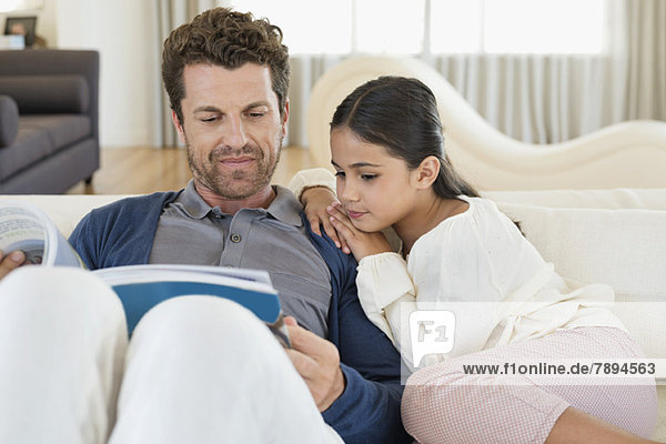 Mann sitzt mit seiner Tochter und liest eine Zeitschrift.