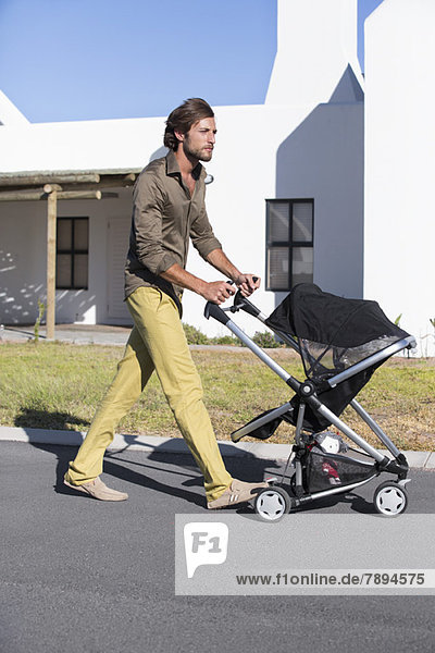 Man pushing a baby stroller on a road