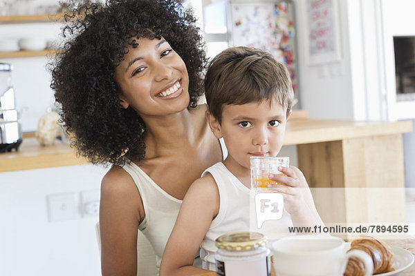 Boy drinking orange juice with his mother sitting with him