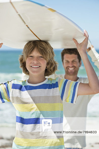 Man and his son carrying a surfboard on the beach