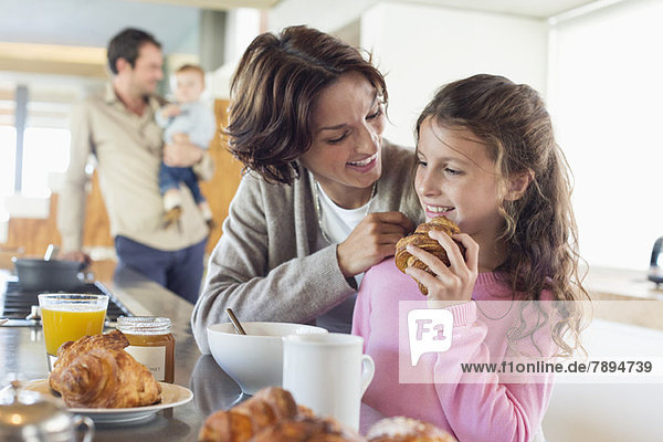 Mädchen frühstückt neben ihrer Mutter an der Küchentheke