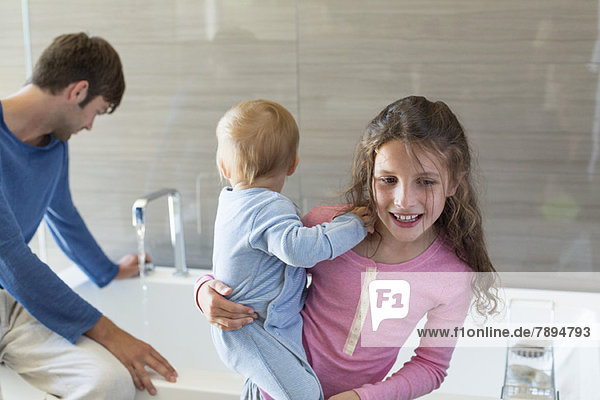 Mädchen lächelt mit ihrem Bruder und ihrem Vater auf einem Wannenrand im Bad.