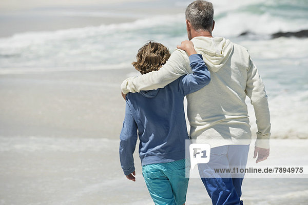 Mann  der mit seinem Enkel am Strand spazieren geht.