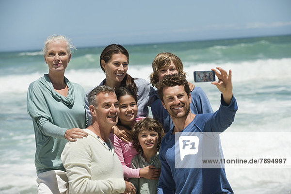 Glückliche Mehrgenerationen-Familie beim Selbstporträt mit dem Handy am Strand