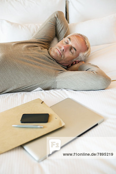 Man resting on the bed with a laptop and file in a hotel room
