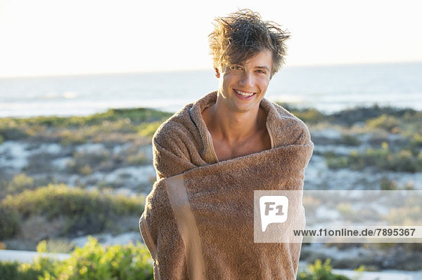 Happy man wrapped in a towel standing on the beach
