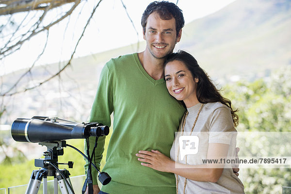 Portrait of a couple smiling beside a binoculars on tripod