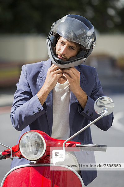 Mann  der auf einem Roller sitzt und einen Helm trägt.