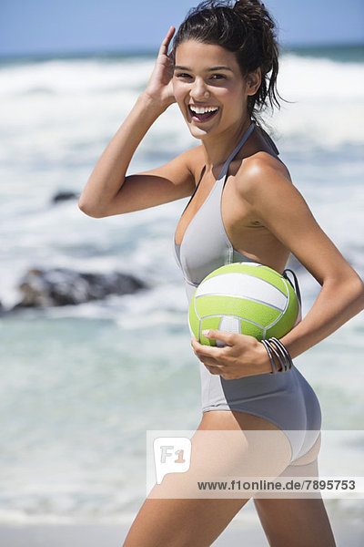 Schöne Frau hält einen Volleyball am Strand.