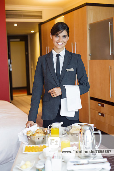 Porträt der lächelnden Kellnerin mit Zimmerservicetisch im Hotelzimmer