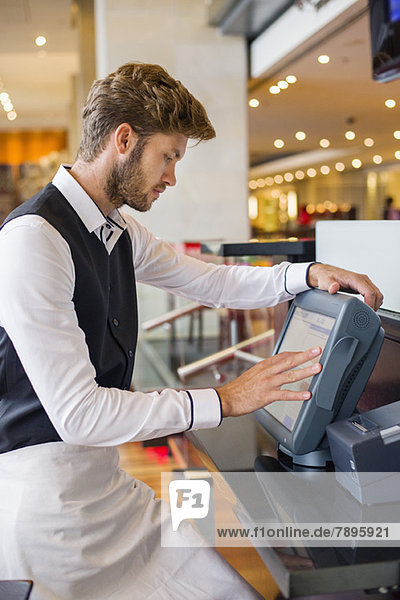 Waiter using a computer at checkout counter in a restaurant
