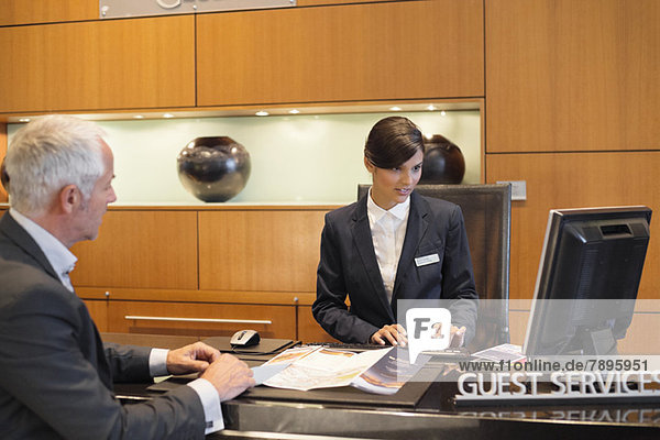 Receptionist working on a desktop pc with a businessman at the hotel reception counter