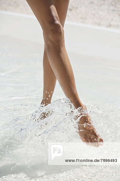 Frau spritzt Wasser mit den Füßen am Strand
