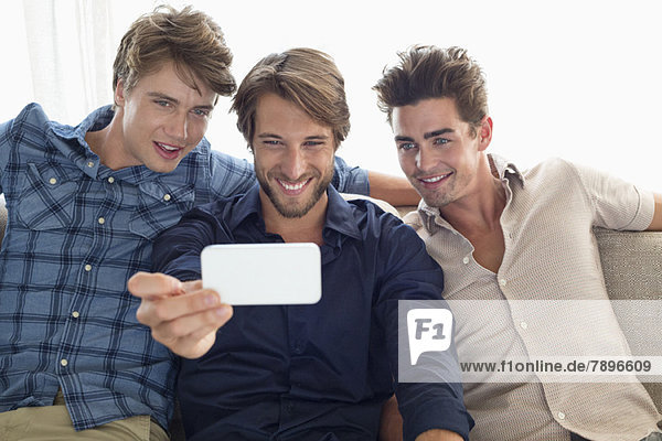 Drei Freunde sitzen auf einer Couch und schauen auf das Handy