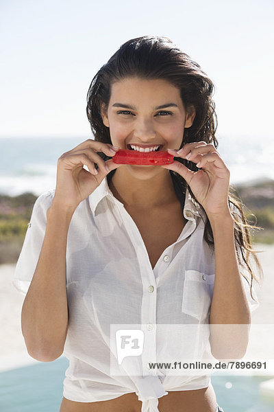 Schöne Frau  die eine Scheibe Wassermelone am Strand isst.