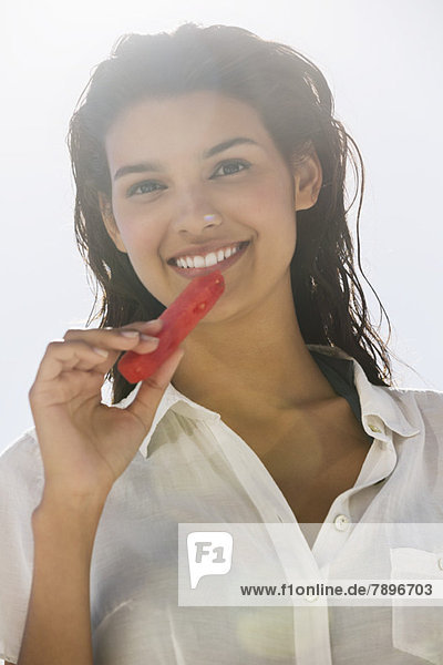 Schöne Frau  die eine Scheibe Wassermelone am Strand isst.