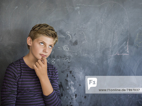 Junge denkt vor einer Tafel in einem Klassenzimmer