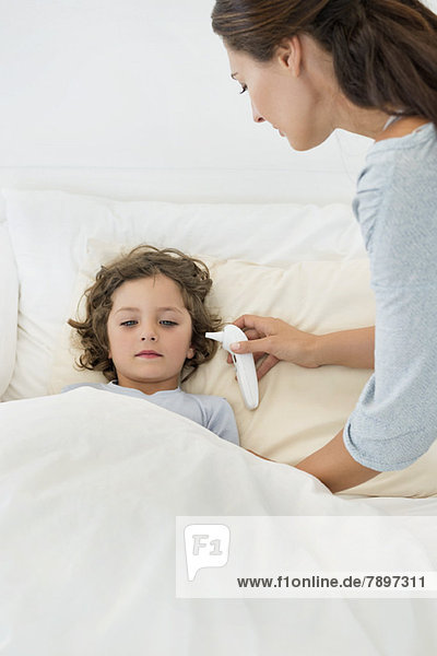 Frau überprüft Fieber ihres Sohnes mit einem Thermometer