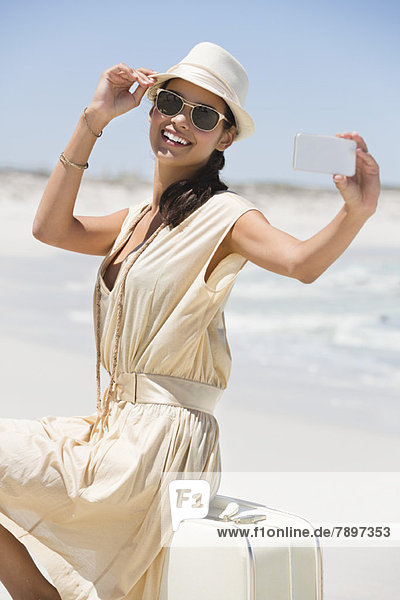 Schöne Frau  die ein Foto von sich selbst mit einem Handy am Strand macht.