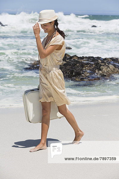 Schöne Frau mit Koffer am Strand