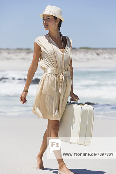 Beautiful woman carrying a suitcase on the beach