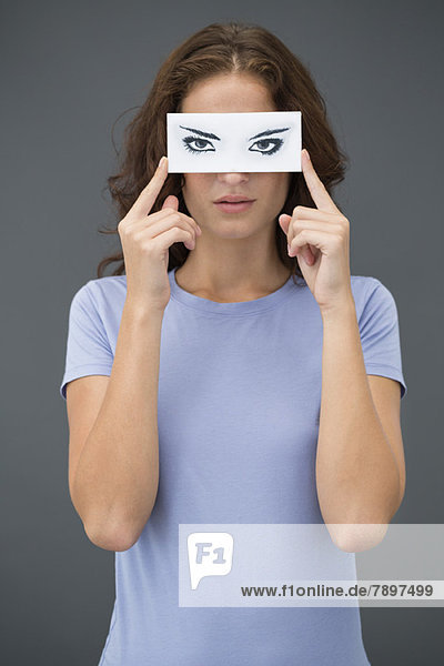 Frau  die ein Papier mit falschen Augen vor ihrem Gesicht hält.